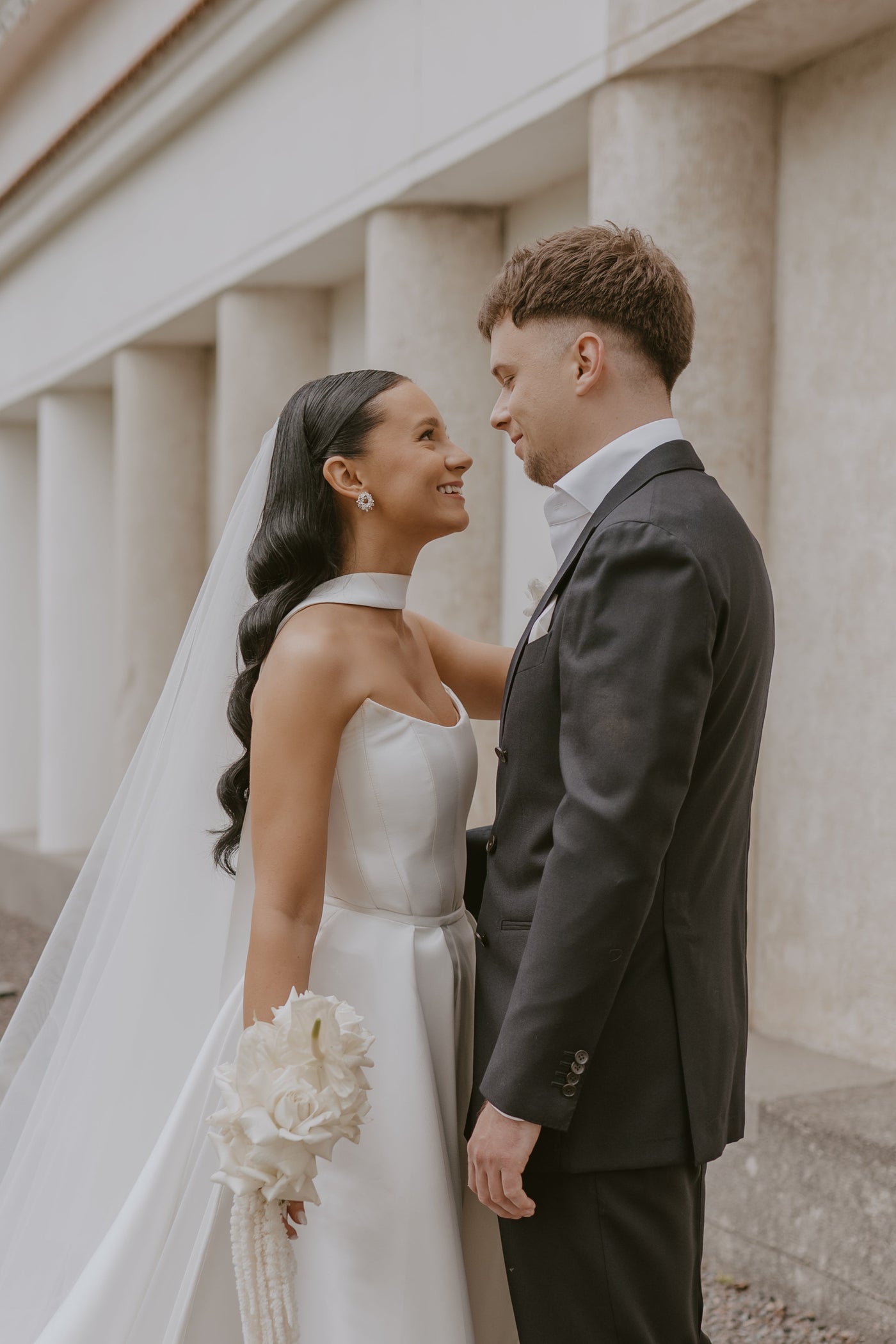 Couple in wedding attire standing close together outdoors.