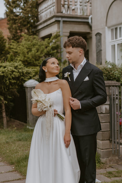 Couple in wedding attire standing in front of a residential building.