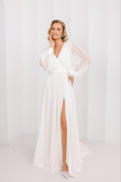 Woman wearing a white dress with a high slit on a plain background