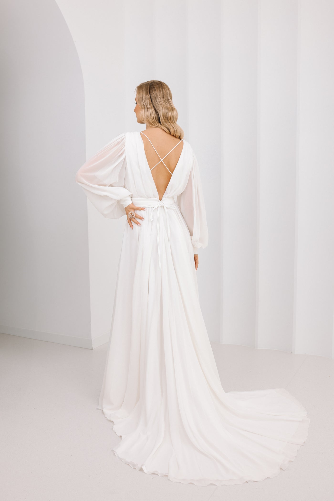 Woman wearing a white wedding dress with a flowing train against a plain background