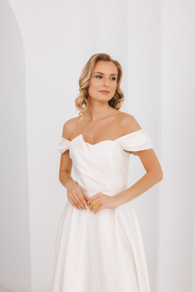 Woman wearing a white off-shoulder dress against a plain background